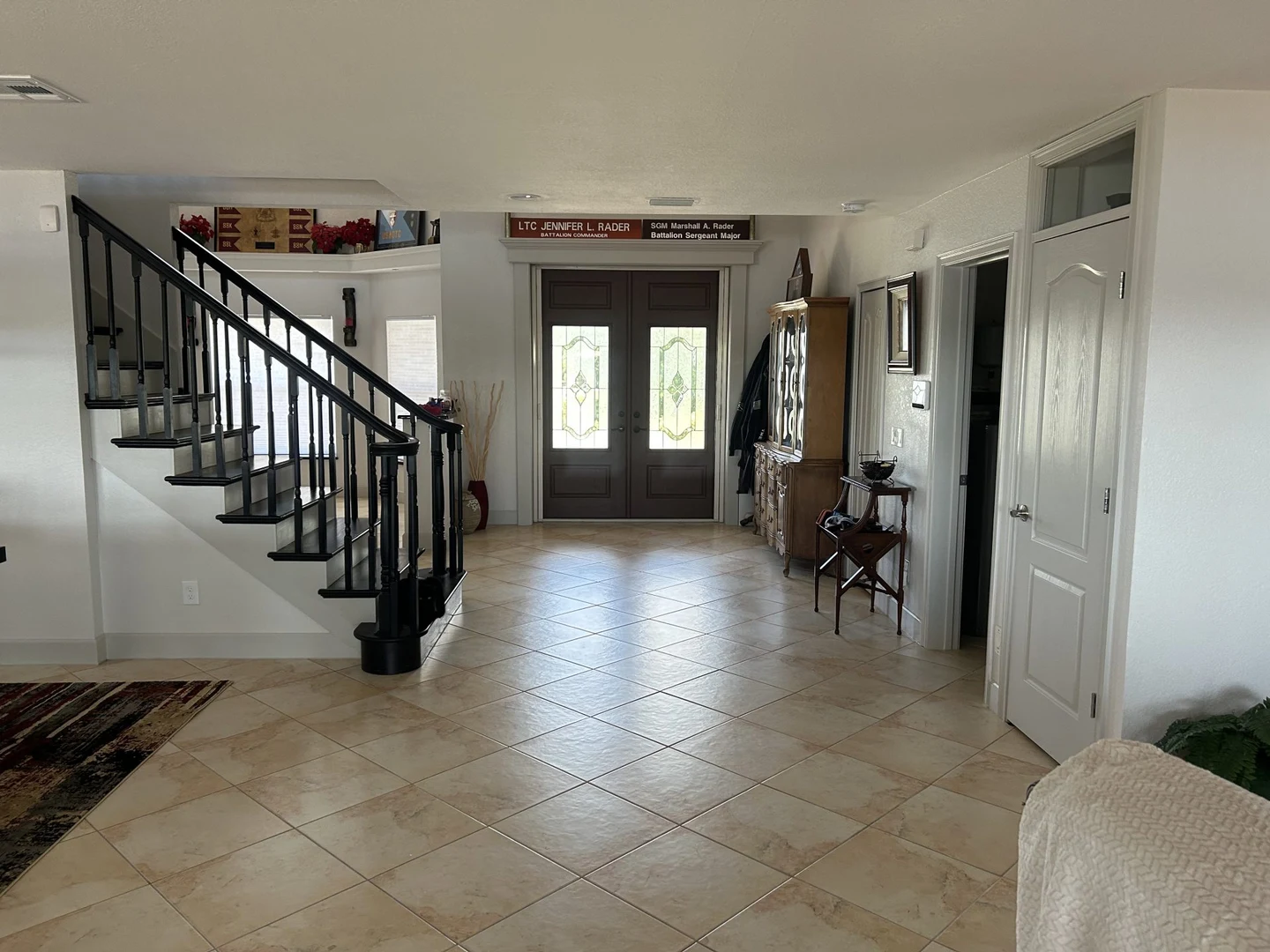 Entry and living area with tile flooring, dark stair railings and glazed front doors.