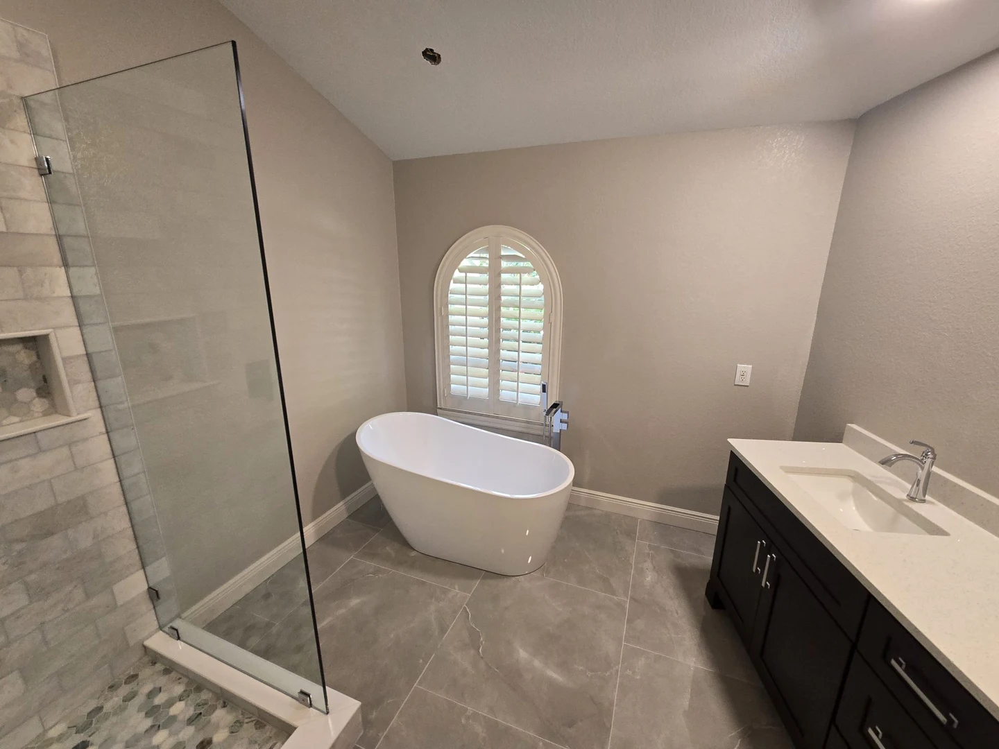 Bathroom with a freestanding white bathtub beneath an arched window and a dark vanity.