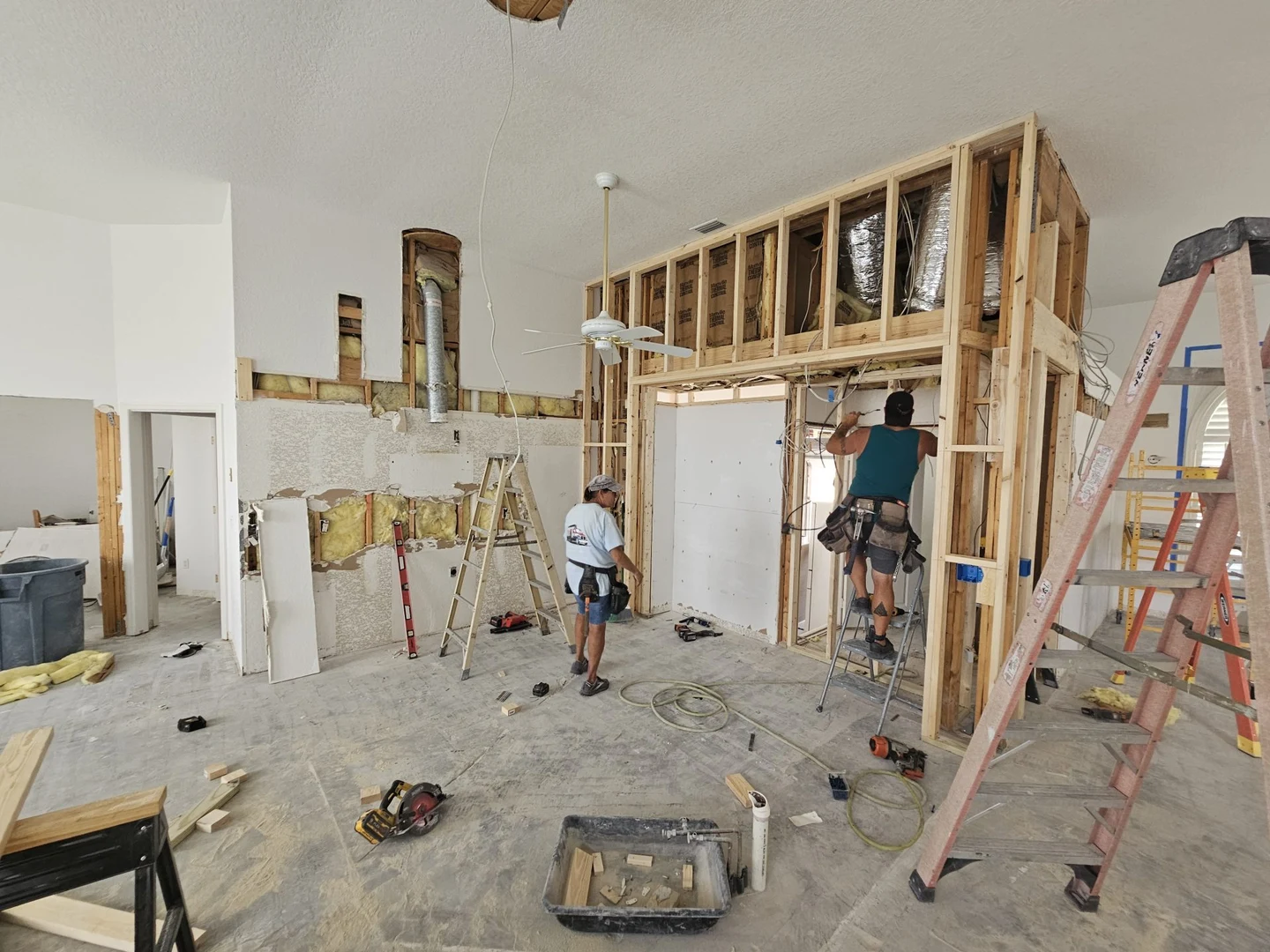Interior renovation in progress, showing exposed wall framing, ladders and construction materials.