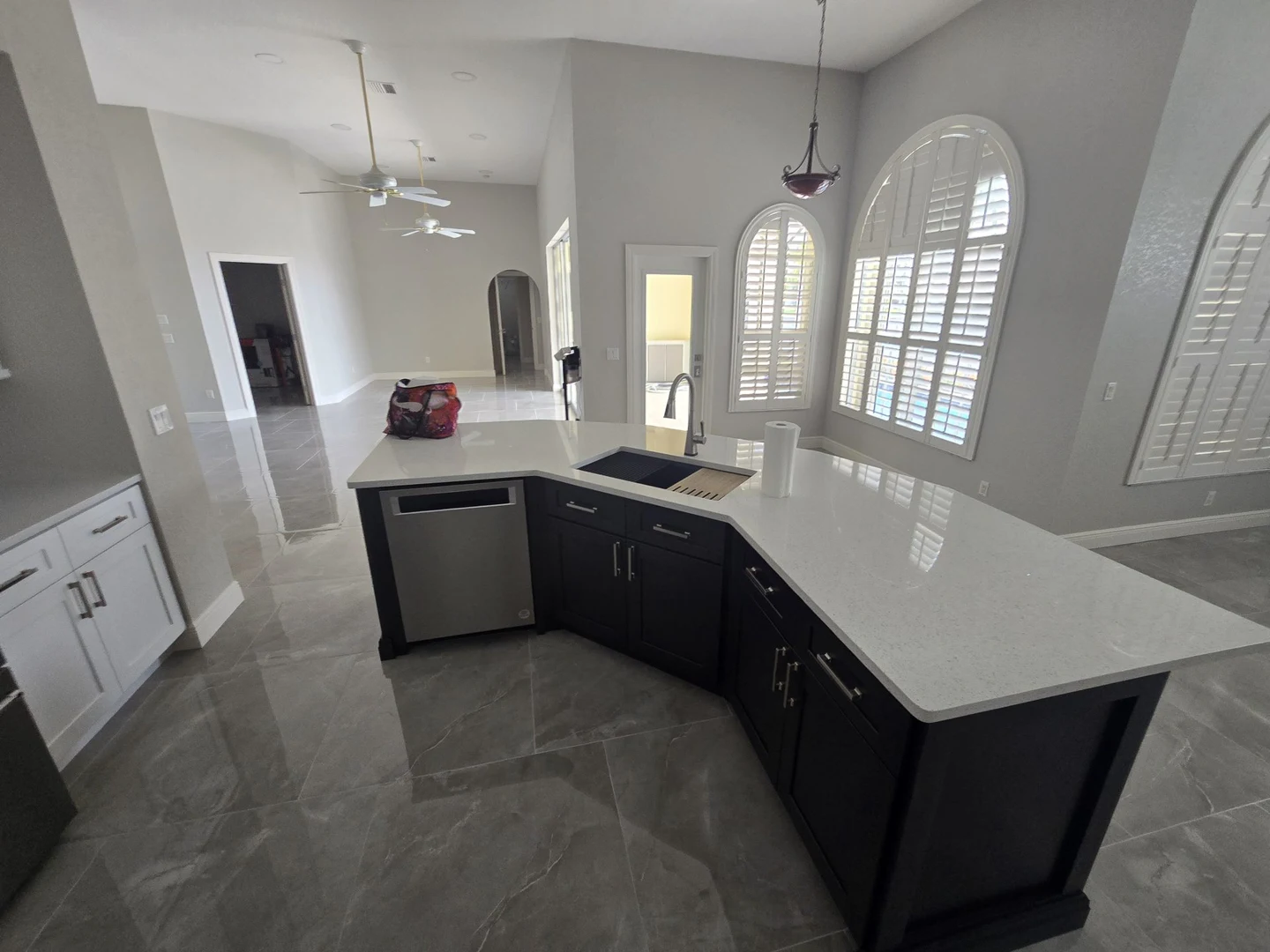 Kitchen with a dark island, white worktop, pendant lighting and large-format gray floor tile.