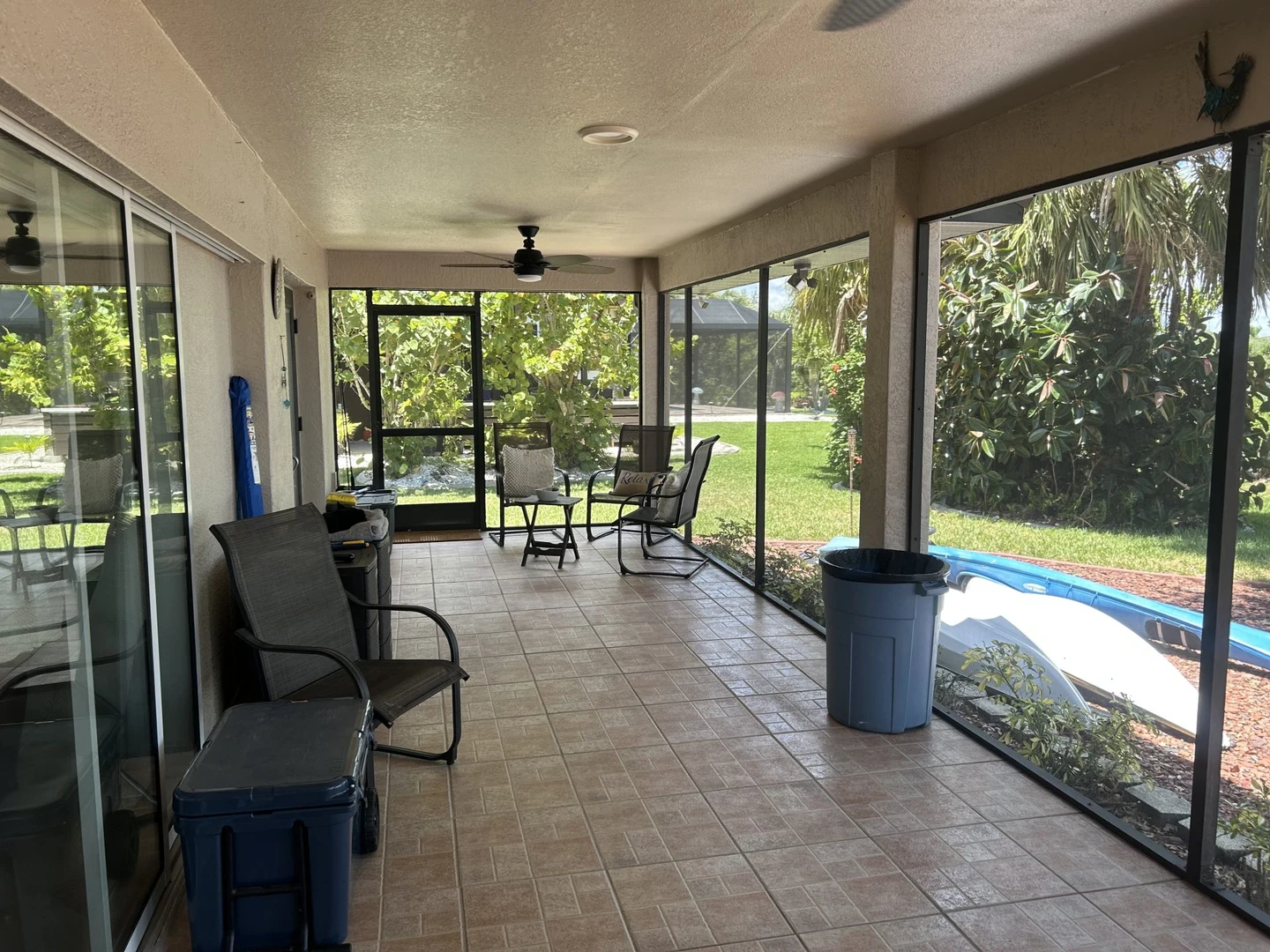 Covered screened porch with tiled flooring, seating and a view of surrounding greenery.