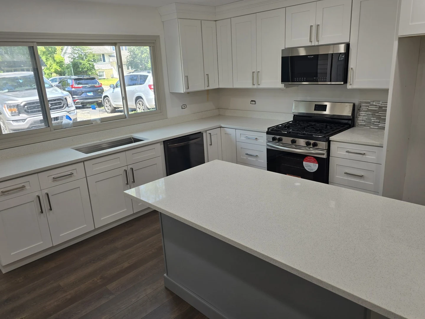 White kitchen cabinetry, pale counters, a tiled backsplash and stainless steel appliances.